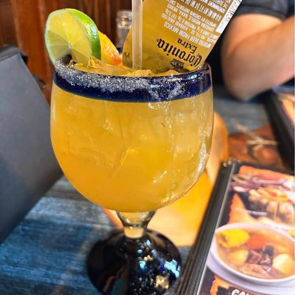 A large margarita glass with a yellow drink, lime, and an inverted Coronita beer.