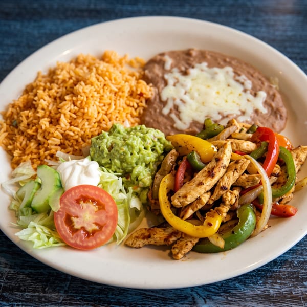 Chicken fajitas with rice, refried beans, guacamole, and a side salad on a white plate.