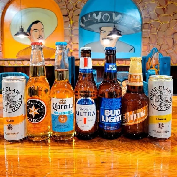 Various beers and hard seltzers displayed on a glossy wooden table with vibrant Mexican-themed murals.