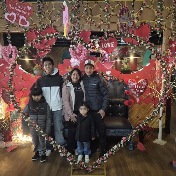 Family of five posing in a restaurant decorated with a large heart arch for Valentine's Day.
