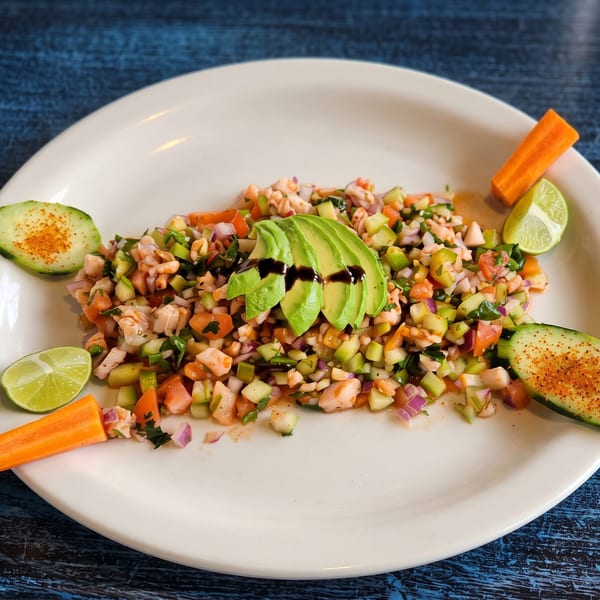 A vibrant plate of shrimp ceviche with diced vegetables, avocado, lime, and spiced cucumber slices.