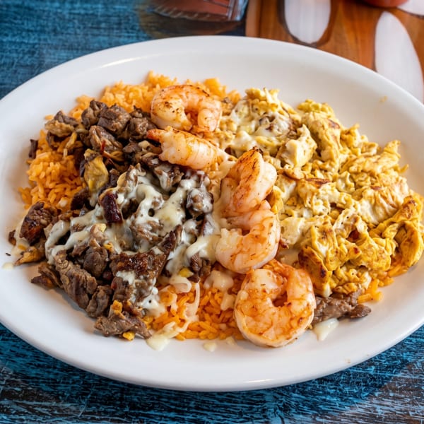 White plate with orange rice, diced beef, shrimp, and scrambled eggs topped with white sauce.
