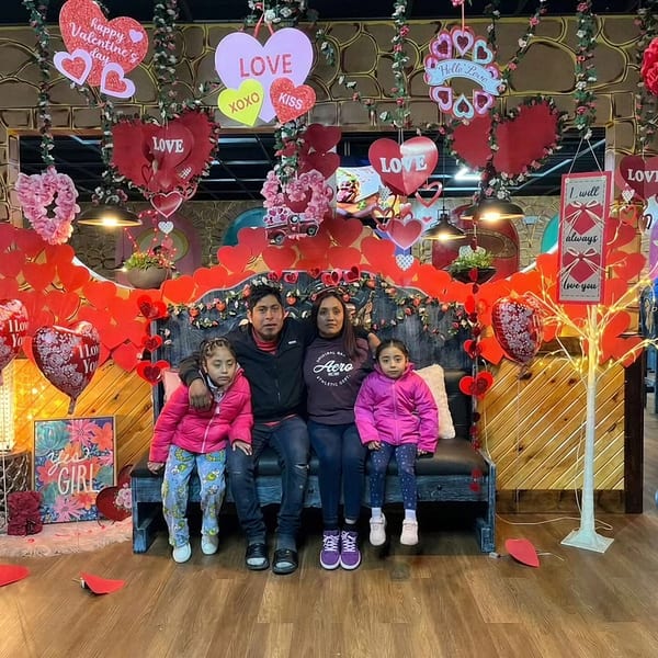 Family of four sitting on a bench in a restaurant decorated with many Valentine's Day hearts.
