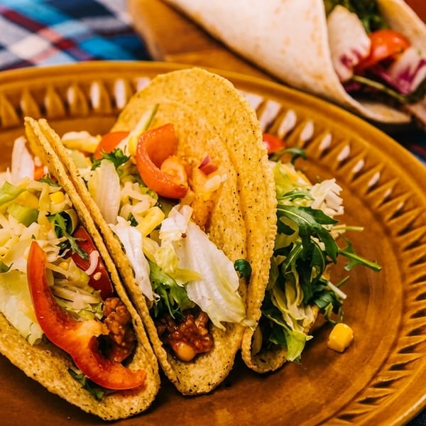 Three hard-shell tacos filled with meat, cheese, lettuce, and tomatoes on a brown plate.