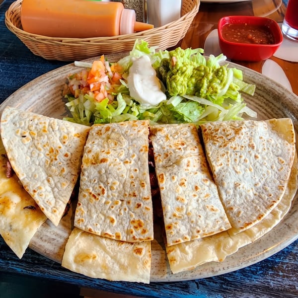 Quesadillas served with a fresh side salad, guacamole, sour cream, and salsa on a blue table.