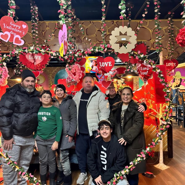 A group of people posing in a restaurant decorated with Valentine's Day hearts and floral garlands.