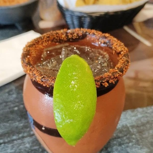 Spiced rimmed drink in a terracotta mug with a lime wedge, chips, and salsa.